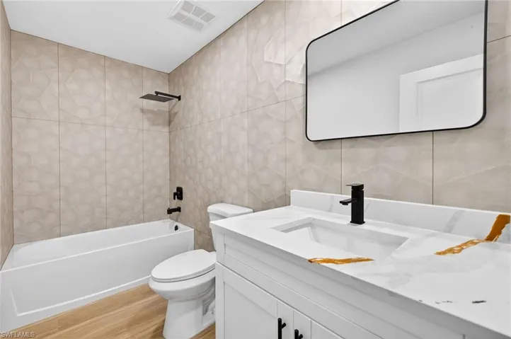 Bathroom with tile walls,  shower combination, vanity, and light wood-type flooring