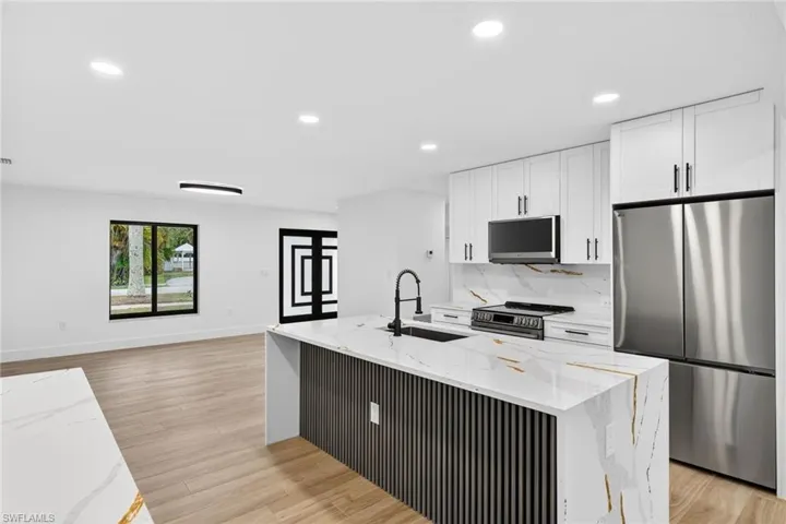 Kitchen with stainless steel appliances, light stone counters, white cabinets, an island with sink, and recessed lighting