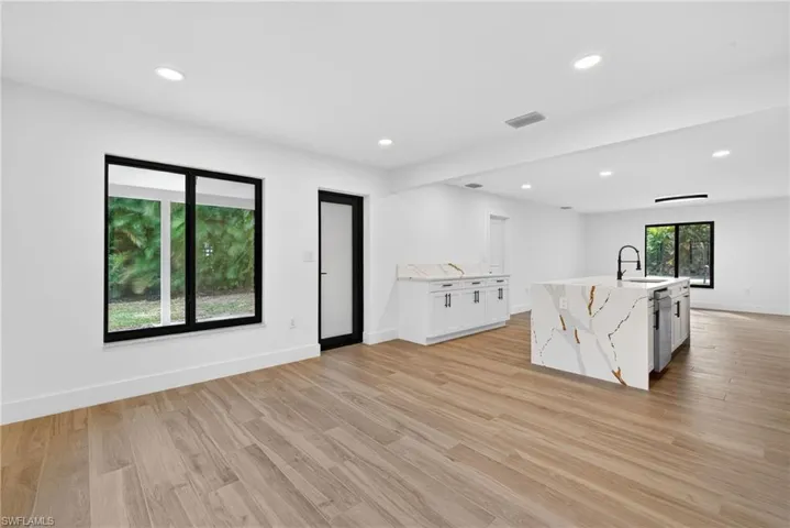 Kitchen with white cabinetry, light stone counters, light wood finished floors, recessed lighting, and an island with sink
