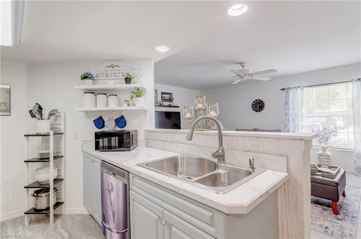 Kitchen with dishwasher, a sink, a peninsula, light countertops, and a ceiling fan