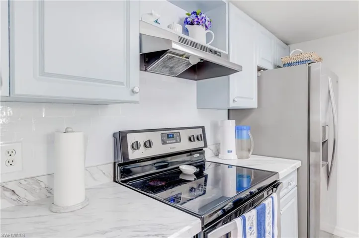 Kitchen featuring stainless steel range with electric stovetop, white cabinets, under cabinet range hood, and light stone countertops