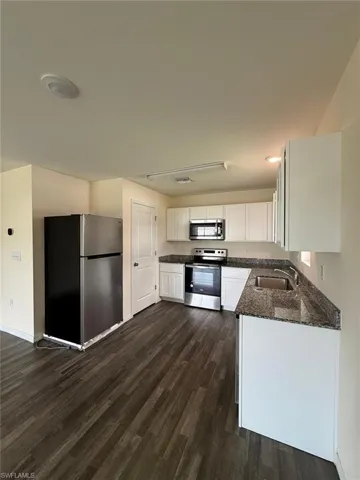 Modern kitchen featuring wood-finish flooring, white cabinetry, granite-style countertops, stainless steel appliances, and a double-basin sink