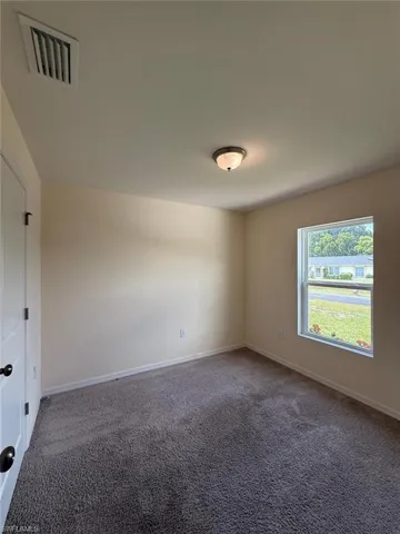 Carpeted room featuring a white paneled door with black hardware, a single window, and a flush-mount ceiling light fixture
