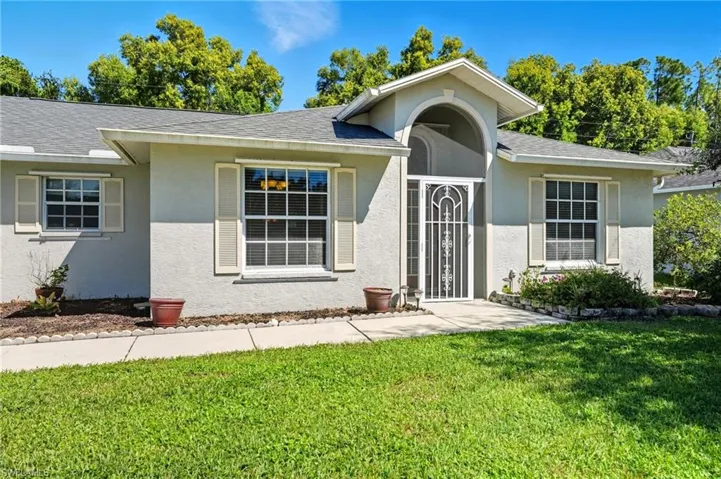 Ranch-style home featuring a front lawn, a shingled roof, and stucco siding