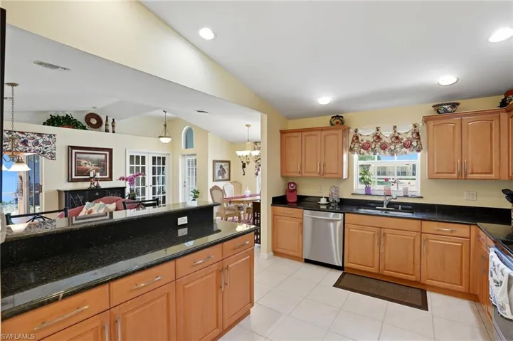 Kitchen with dark stone countertops, hanging light fixtures, stainless steel dishwasher, lofted ceiling, and light tile patterned floors