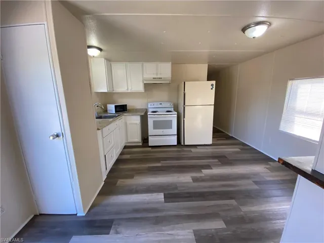 Kitchen featuring white cabinets, white appliances, light countertops, and dark wood-style flooring