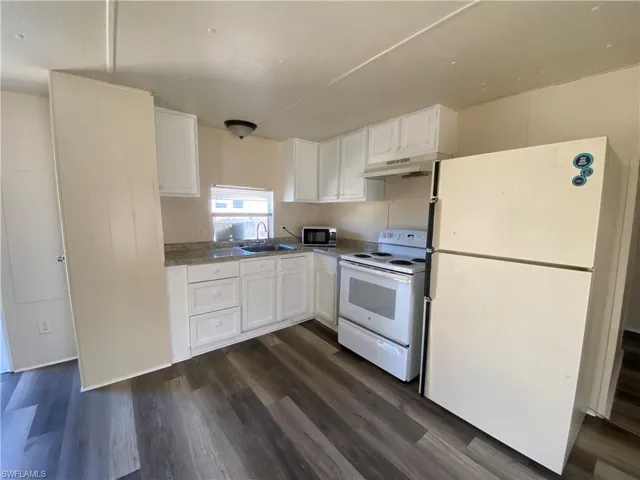 Kitchen featuring white appliances, white cabinetry, dark wood-style flooring, and light countertops