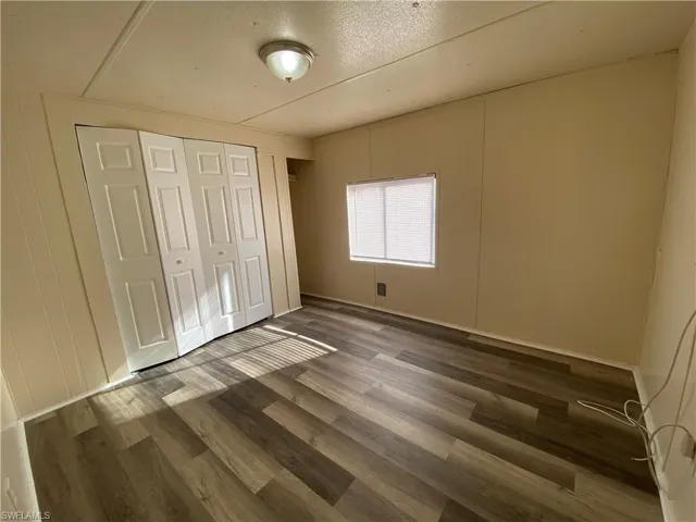 Unfurnished bedroom featuring a closet, a textured ceiling, dark wood-style flooring, and a decorative wall