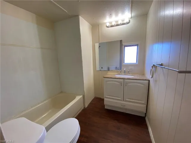 Full bathroom with vanity, dark wood-type flooring, wooden walls, and a textured ceiling