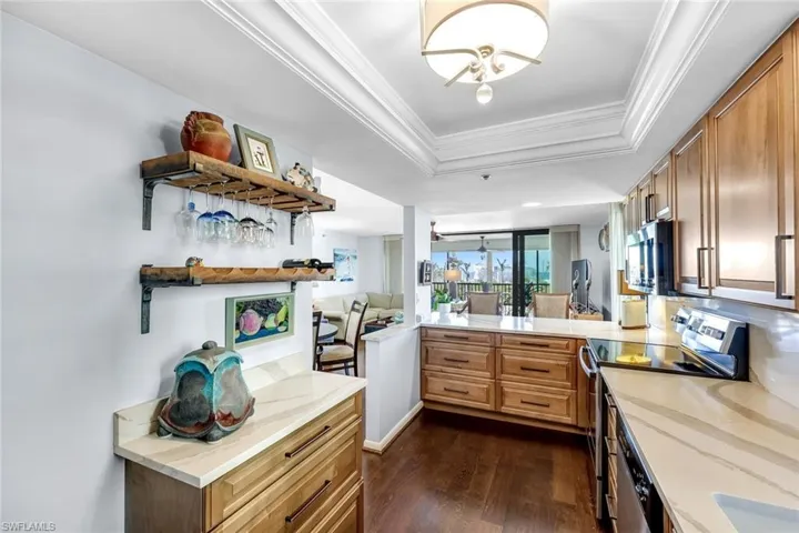 Wood-finish flooring with light wood cabinetry, stone countertops, stainless steel appliances, and a built-in wine rack