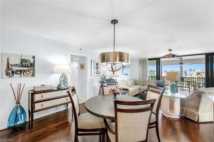 Hardwood-finish flooring, a contemporary drum pendant light fixture, a wood-finish dining table with upholstered chairs, and multi-panel sliding glass doors to the exterior