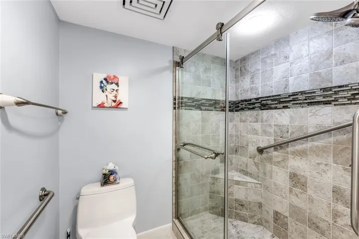 Glass-enclosed shower with a mosaic tile accent band, integrated corner shelf, and brushed nickel fixtures