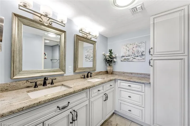 Dual vanity with undermount sinks, stone countertops, white shaker-style cabinetry, and oil-rubbed bronze hardware