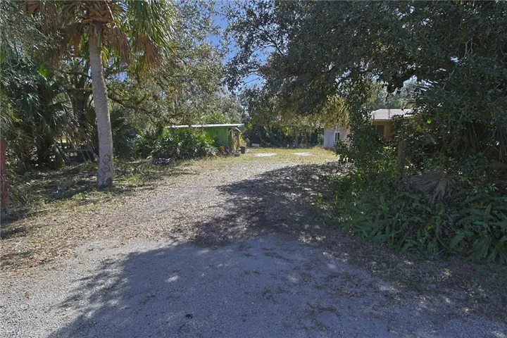 Gravel driveway leading to a partially visible structure with a metal roof and a separate green outbuilding