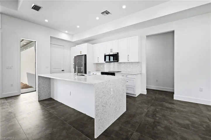 Kitchen featuring stainless steel appliances, a kitchen island with sink, white cabinets, backsplash, and recessed lighting