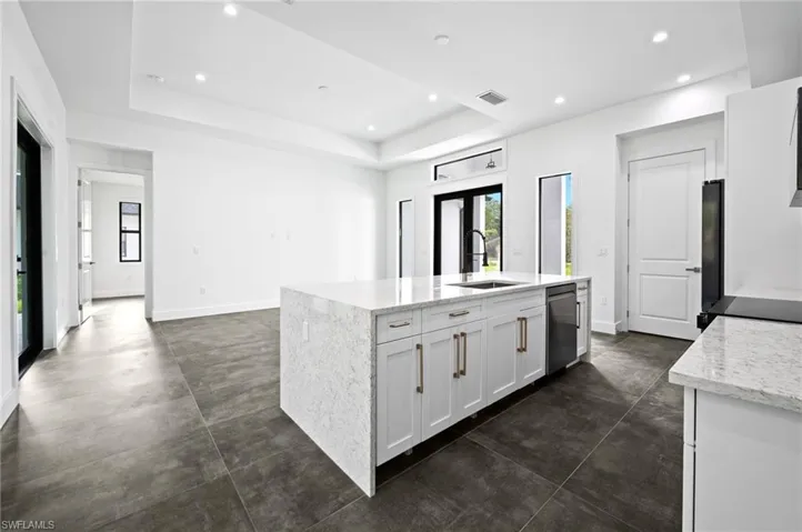 Kitchen with dishwasher, a kitchen island with sink, a raised ceiling, recessed lighting, and white cabinetry