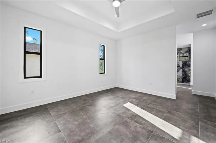 Empty room featuring ceiling fan, concrete flooring, and a tray ceiling