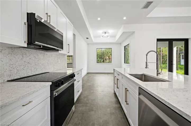 Kitchen with appliances with stainless steel finishes, a raised ceiling, decorative backsplash, light stone countertops, and white cabinets