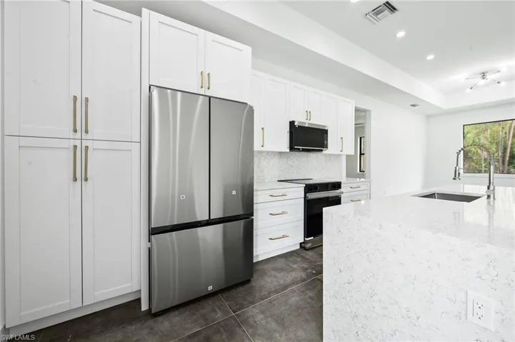 Kitchen featuring stainless steel fridge, range with electric stovetop, white cabinets, light stone countertops, and backsplash