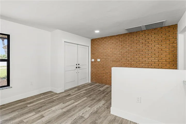 Accent brick wall with wood-finish flooring, white double bifold doors, and modern recessed lighting