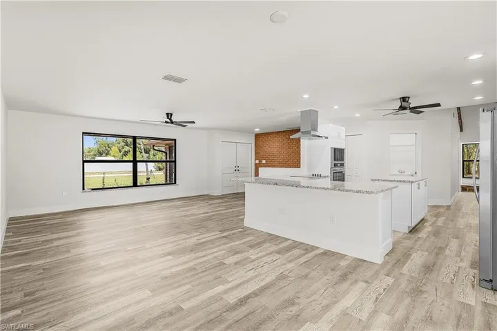 Spacious open-concept interior featuring light wood-finish flooring, recessed lighting, and ceiling fans