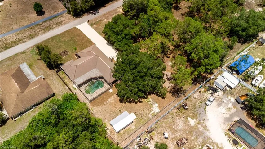 Aerial view showcasing a property with a private fenced swimming pool, expansive driveway, and mature trees