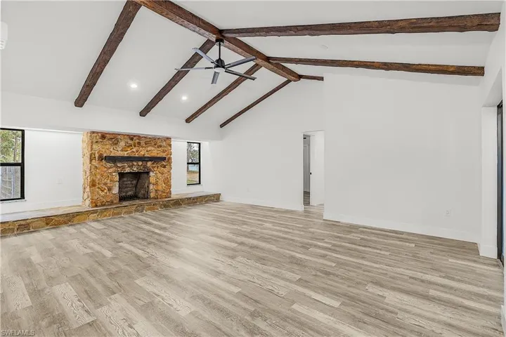 Spacious living area featuring a vaulted ceiling with exposed wood beams, a stone fireplace with hearth, recessed lighting, and wood-finish flooring