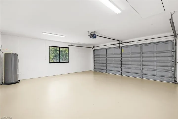 Spacious garage featuring a light-colored epoxy floor, a paneled garage door, fluorescent overhead lighting, a mounted water heater, and a horizontal window