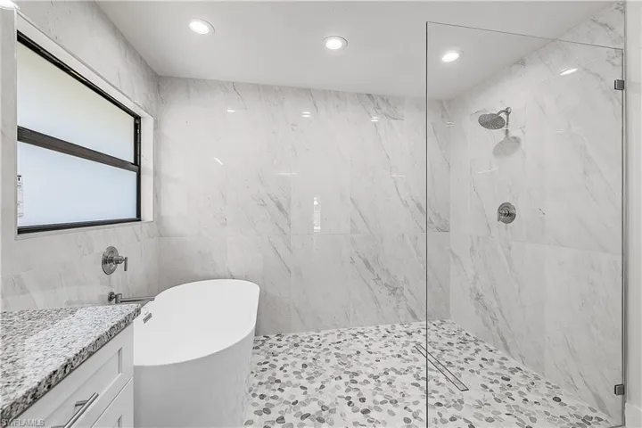 Modern bathroom featuring a freestanding soaking tub, frameless glass shower enclosure, natural stone pebble shower floor, and a window with frosted glass