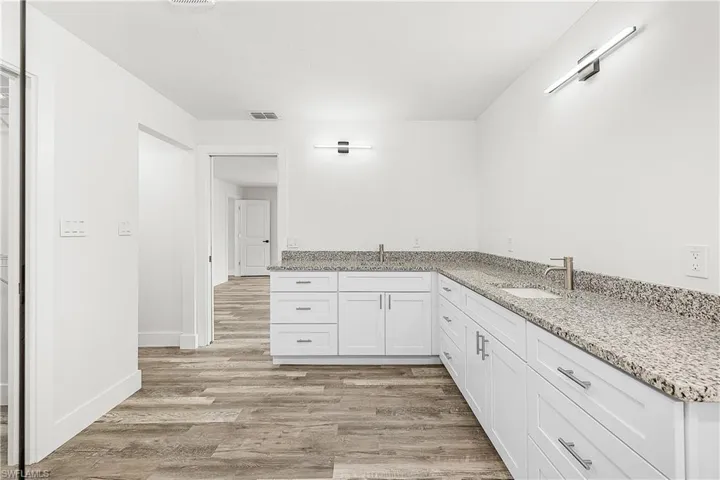 Spacious bathroom featuring a dual vanity with light-toned stone countertops, white shaker-style cabinetry, and wood-finish flooring