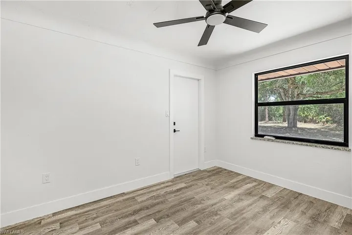 Room featuring wood-finish flooring, a contemporary ceiling fan, a window with a stone sill, and a white interior door