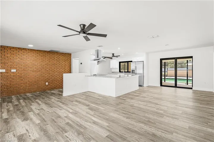 Open-concept living space featuring wood-finish flooring, a brick accent wall, and a kitchen island with stone countertops