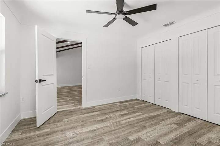 Spacious room featuring wood-finish flooring, a contemporary ceiling fan, and multiple bi-fold closet doors