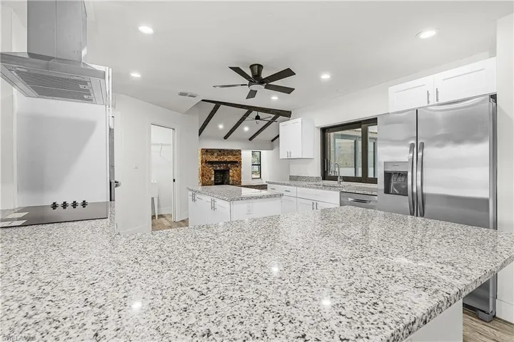 Spacious kitchen featuring extensive granite countertops, white cabinetry, stainless steel appliances, and recessed lighting