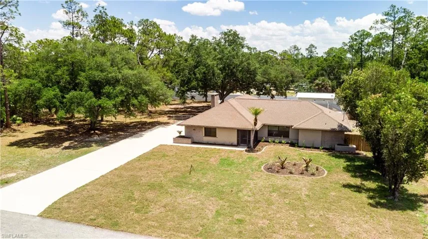 Spacious property featuring a long concrete driveway, mature trees, and landscaped planting beds