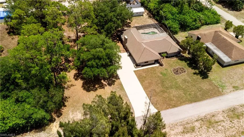 Expansive property featuring a screened-in pool, mature trees, and a paved driveway