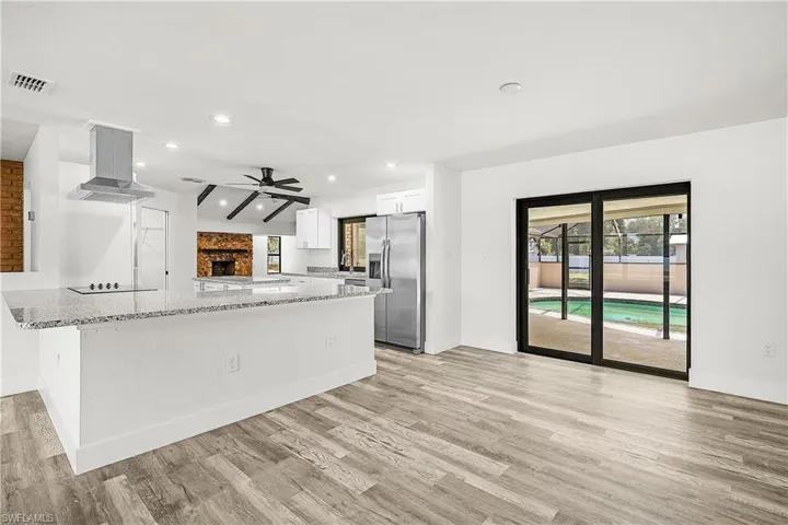 Spacious open-concept living area featuring wood-finish flooring, a contemporary kitchen island with granite countertops, stainless steel appliances, and a built-in electric cooktop