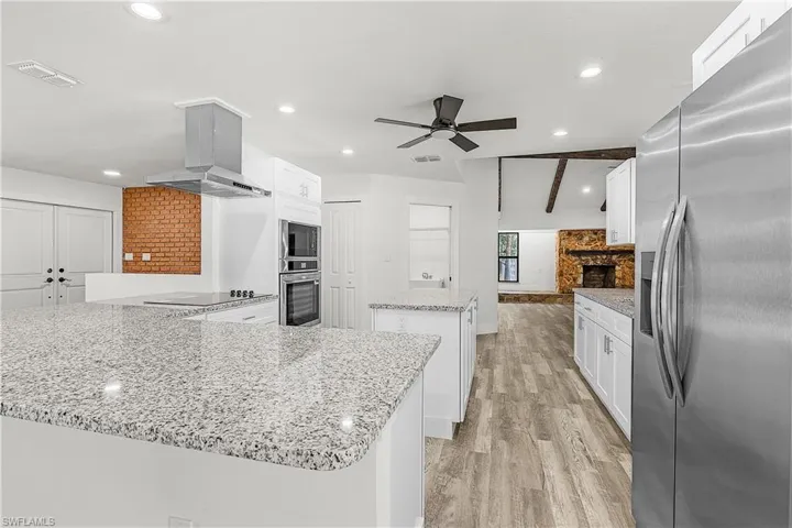 Kitchen featuring granite countertops, white cabinetry, integrated stainless steel appliances, a range hood, and wood-finish flooring
