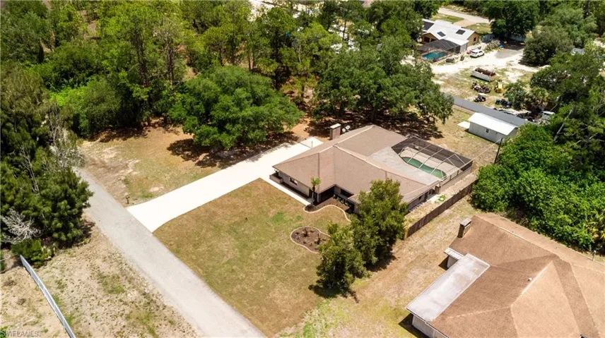 Aerial view of a single-story residence featuring a brown shingle roof, a screened-in swimming pool, and a paved driveway