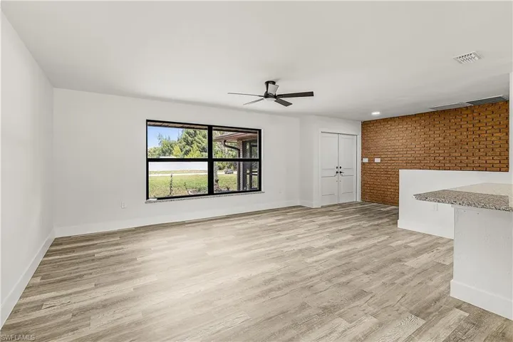 Spacious interior featuring wood-finish flooring, a large window with black framing, a ceiling fan, and a brick accent wall