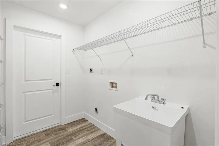 Dedicated utility room featuring a utility sink, recessed lighting, wire shelving, wood-finish flooring, and a white paneled door with matte black hardware