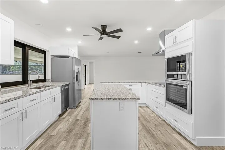 Spacious kitchen featuring white cabinetry, granite countertops, stainless steel appliances, a center island, and wood-finish flooring