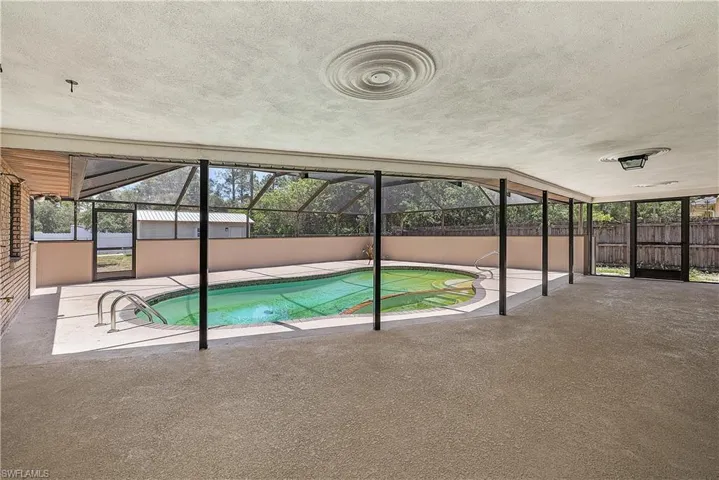 Screened pool enclosure featuring a kidney-shaped pool with integrated steps, surrounded by a textured concrete patio