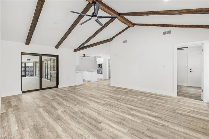 Spacious living area featuring a vaulted ceiling with exposed wood beams, wood-finish flooring, and a modern ceiling fan