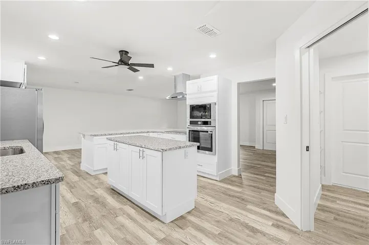 Open-concept kitchen featuring two large islands with granite countertops, stainless steel appliances, a built-in oven, and wood-finish flooring
