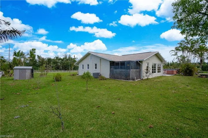 Rear view of house with a shed, a yard, a sunroom, a hot tub, and central air condition unit
