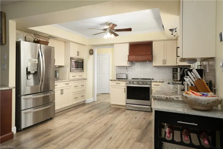 Kitchen featuring premium range hood, appliances with stainless steel finishes, ornamental molding, and white cabinets