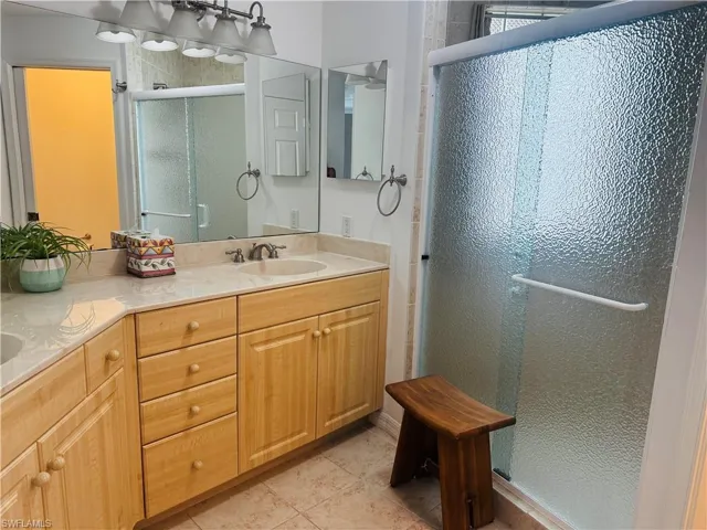 Bathroom with a shower stall, double vanity, and light tile patterned flooring