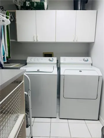 Laundry area featuring light tile patterned floors, washer and clothes dryer, and cabinet space