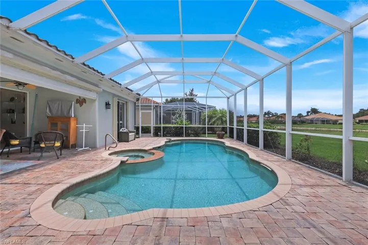 Screened outdoor area featuring a freeform pool with integrated steps, a spa, and brick paver decking